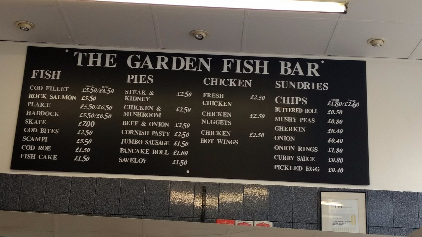 The hand-painted menu board inside The Garden Fish Bar listing fish, pies, chicken and sundries with prices